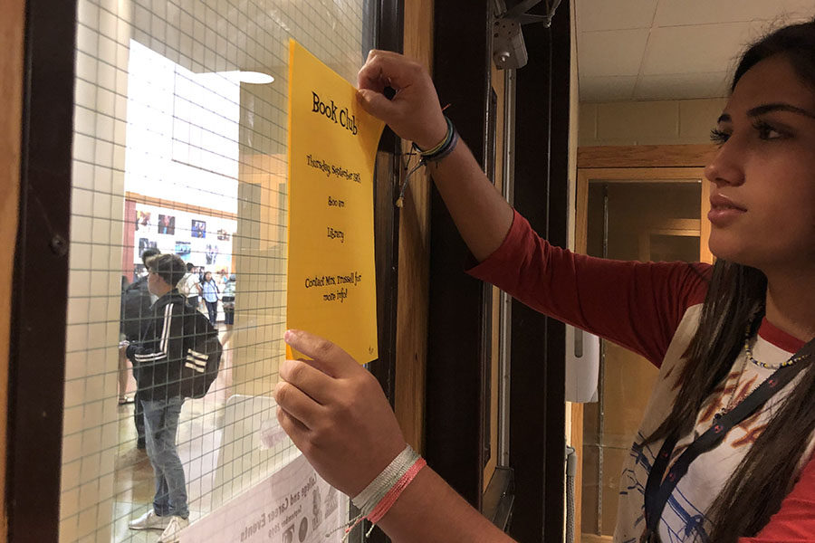 Marissa Meisner, library aide, hangs Book Club sign in the library in preparation for the first meeting 8 a.m. Thursday.