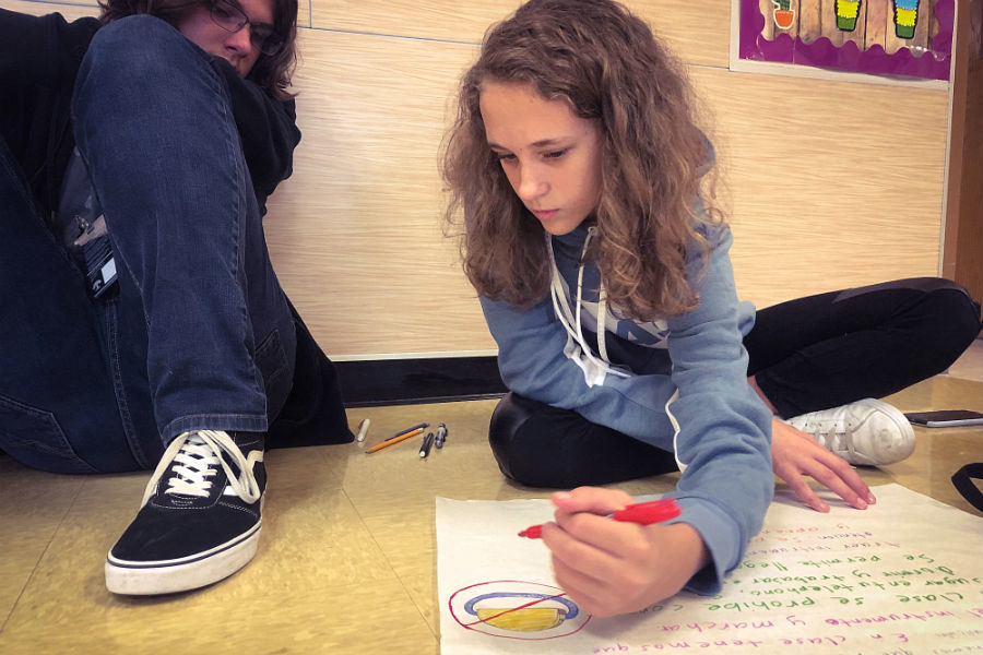 On the floor of the A wing hallway, freshmen Lena Deaver and Zachary Hyde work on a presentation for Spanish.