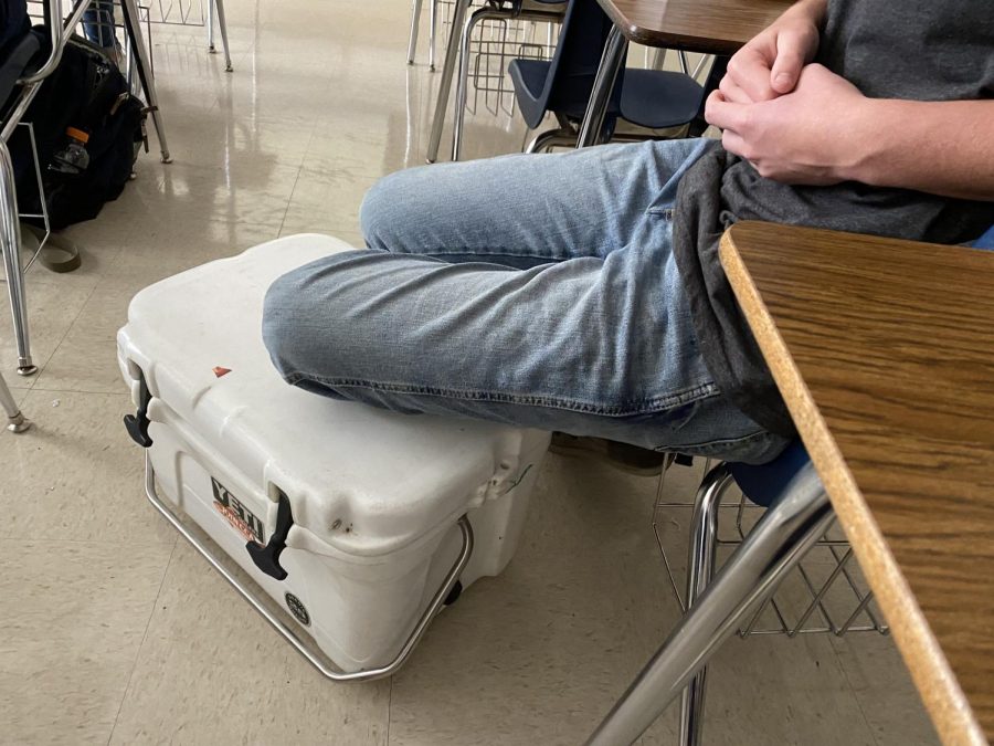 Junior Mason Schroeder rests his feet on the cooler he brought to use as his backpack. This is part of widespread participation in "bring anything but a backpack day."